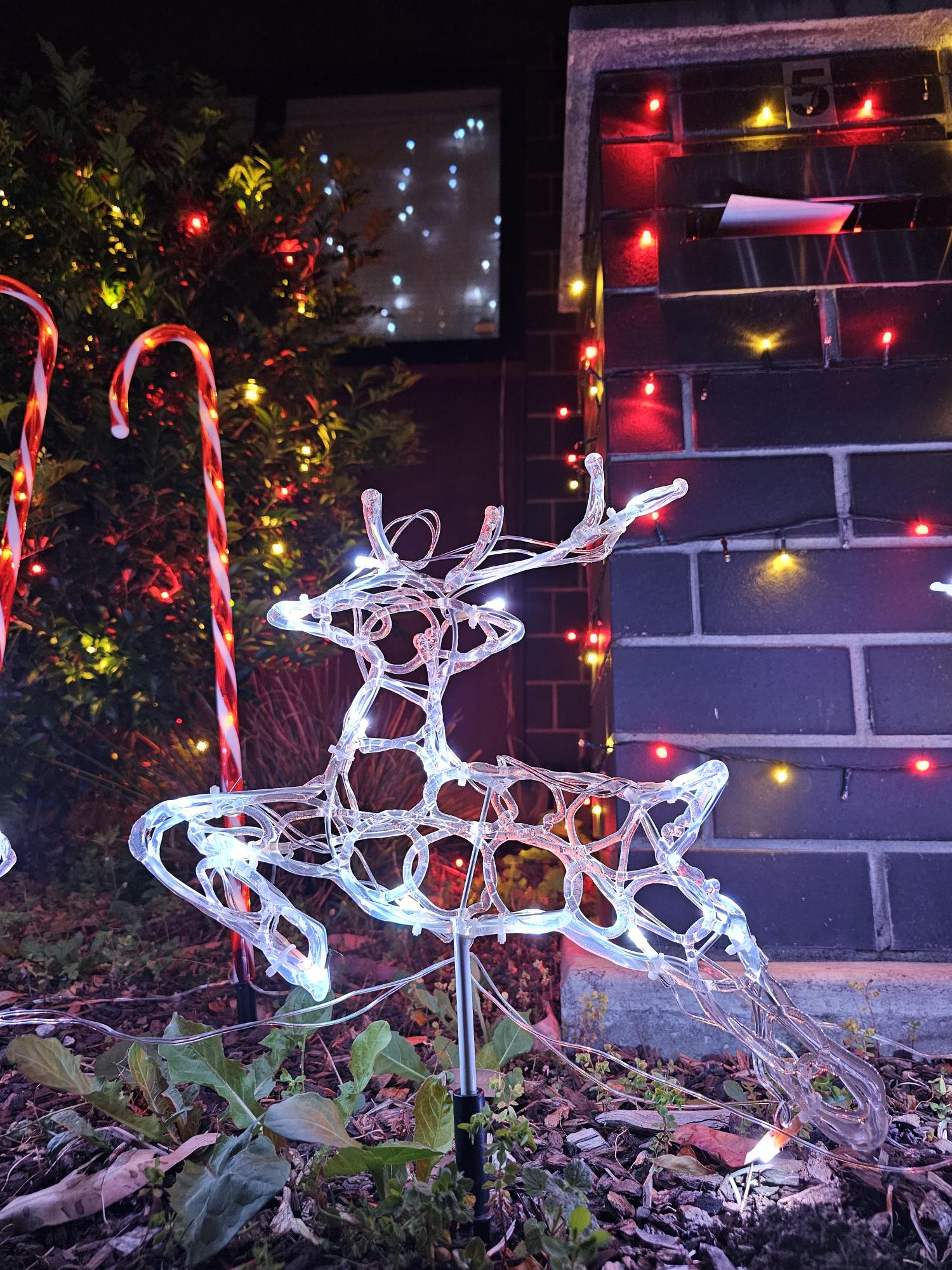 A white illuminated reindeer beside a decorated letterbox